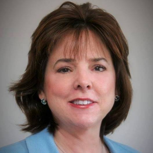 A woman with brown hair and wearing blue is smiling.