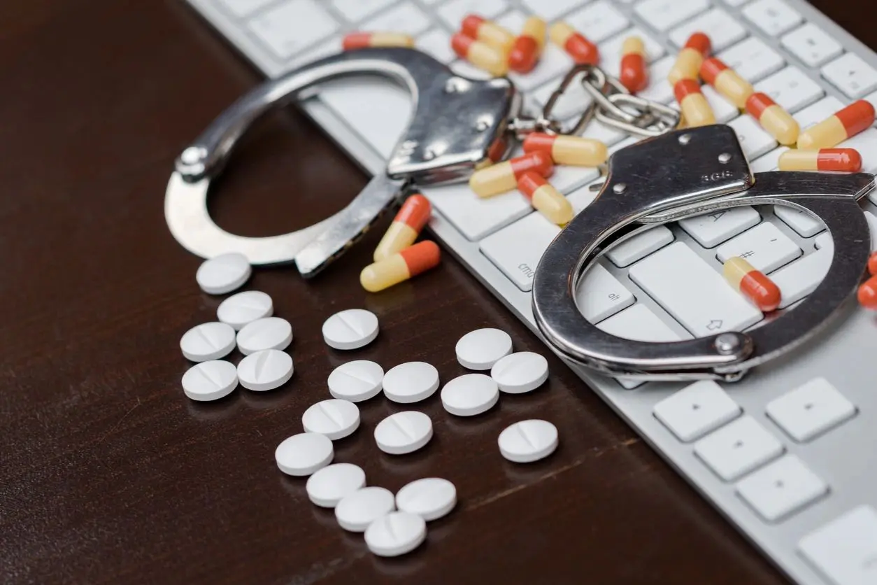 A pair of handcuffs and pills on top of a keyboard.