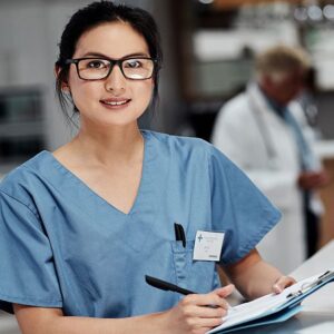 A woman in blue scrubs holding a pen and paper.