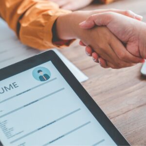 Two people shaking hands over a resume on top of a table.