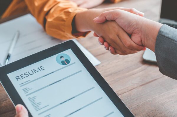 Two people shaking hands over a resume on top of a table.