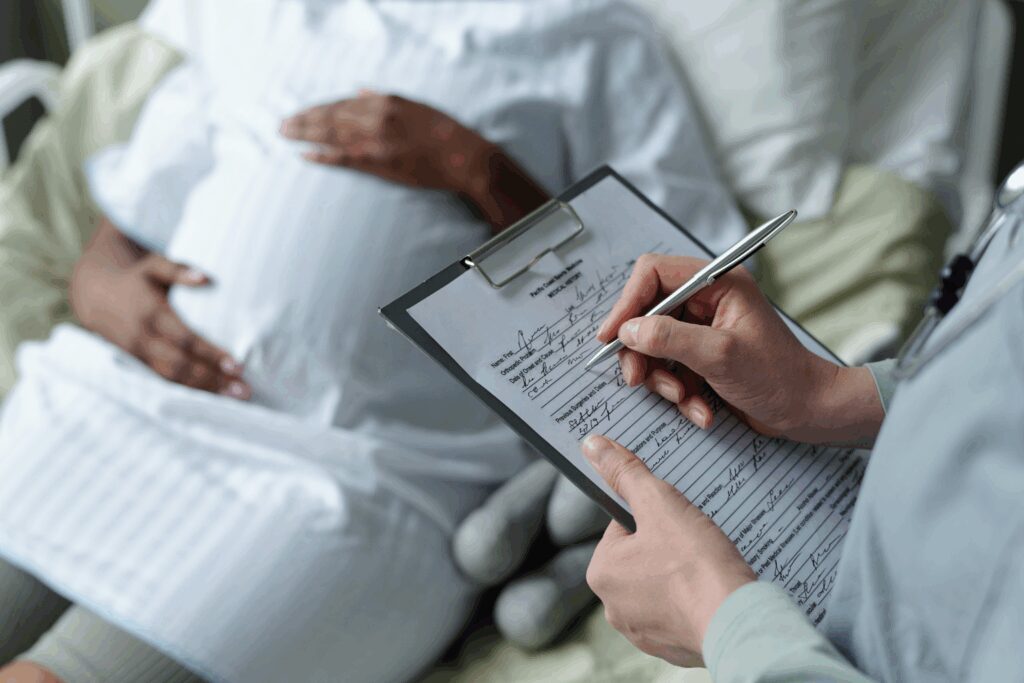 Nurse documenting care for pregnant patient in hospital bed